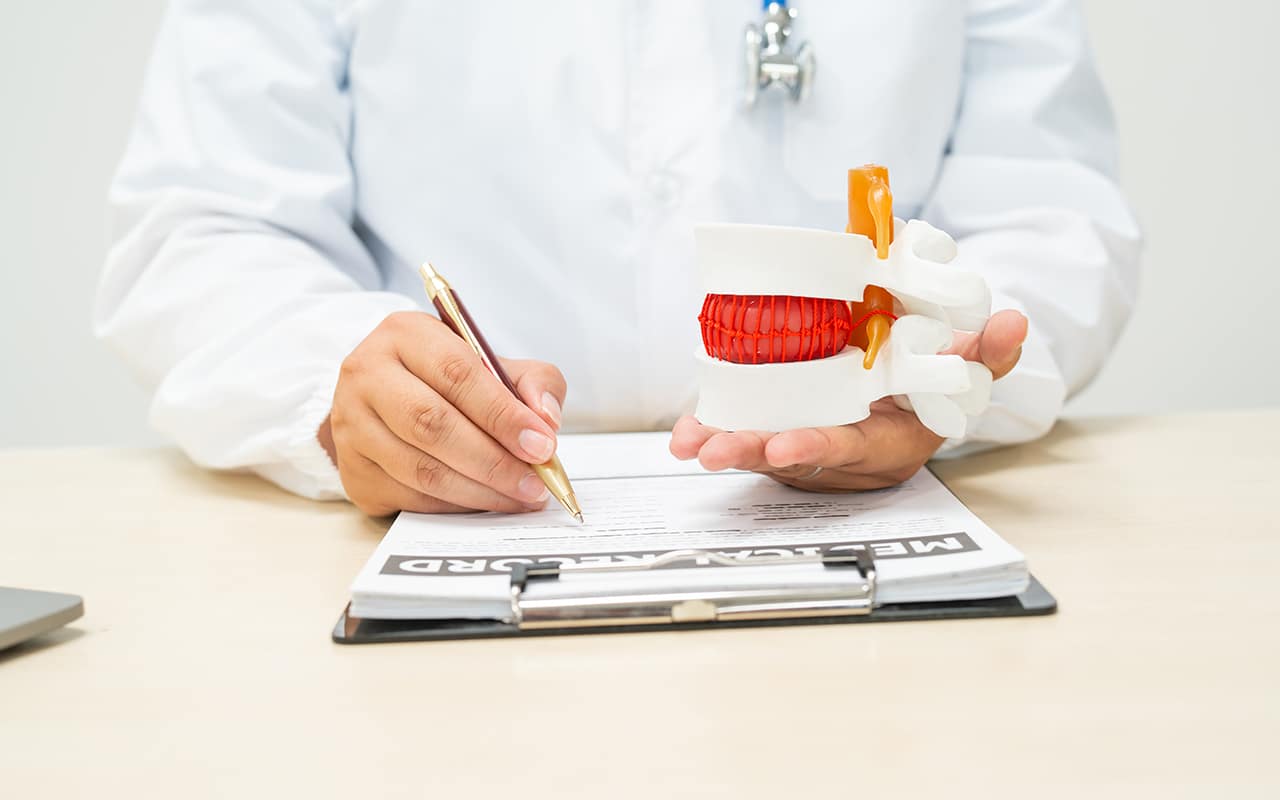 Médico que faz cirurgias minimamente invasivas da coluna segurando um modelo de vértebra e fazendo anotações - site Dr. Marcio Penna cirurgião de coluna de Belém - PA