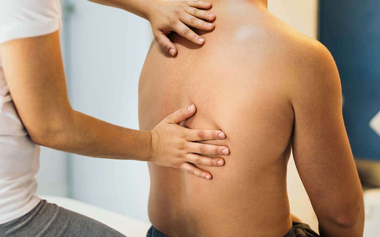 Fisioterapeuta examinando jovem com dor nas costas na parte de cima das costas - site Dr. Marcio Penna ortopedista especialista em coluna