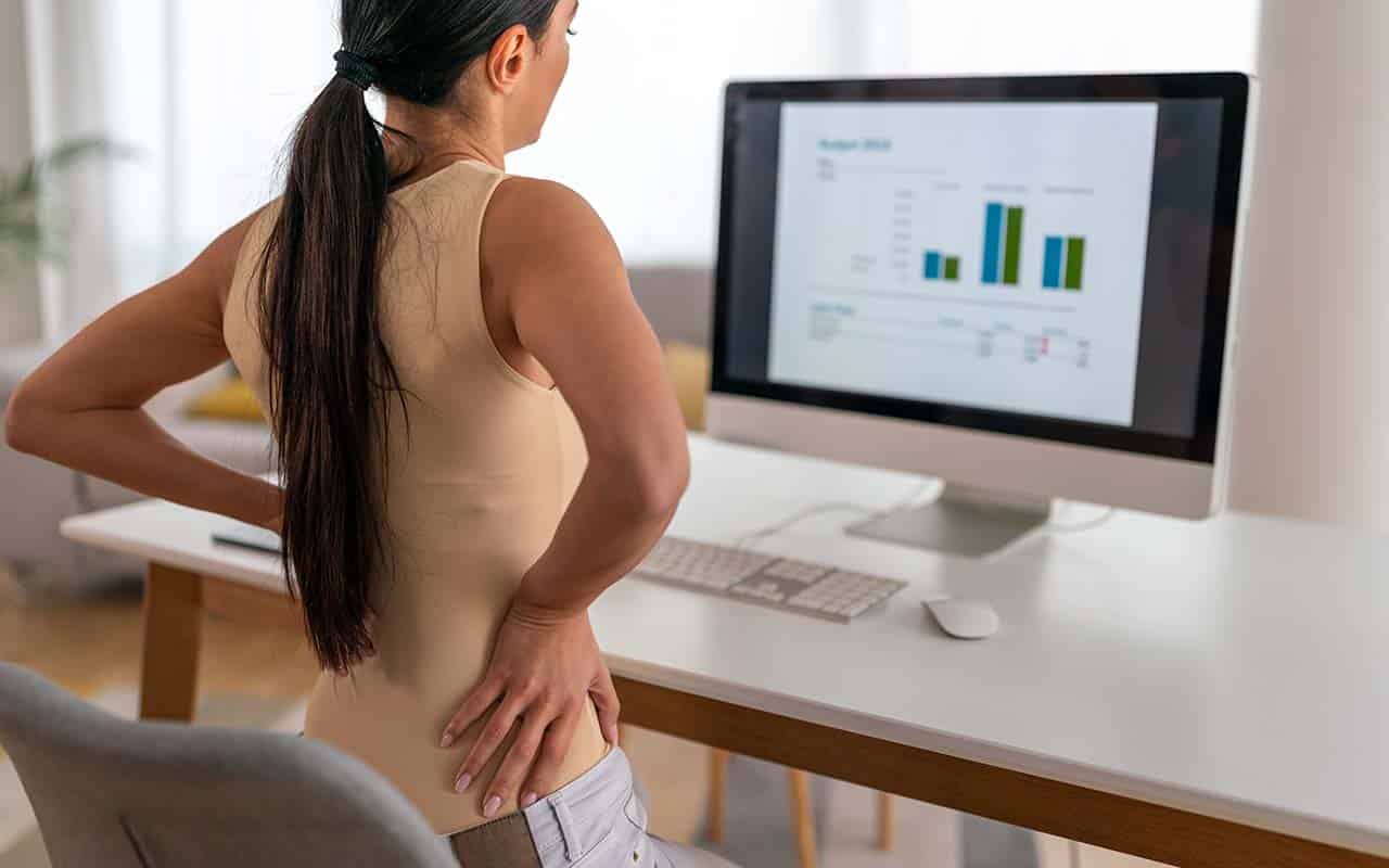 Mulher em frente ao computador com dor na lombar - site Dr. Marcio Penna ortopedista especialista em coluna