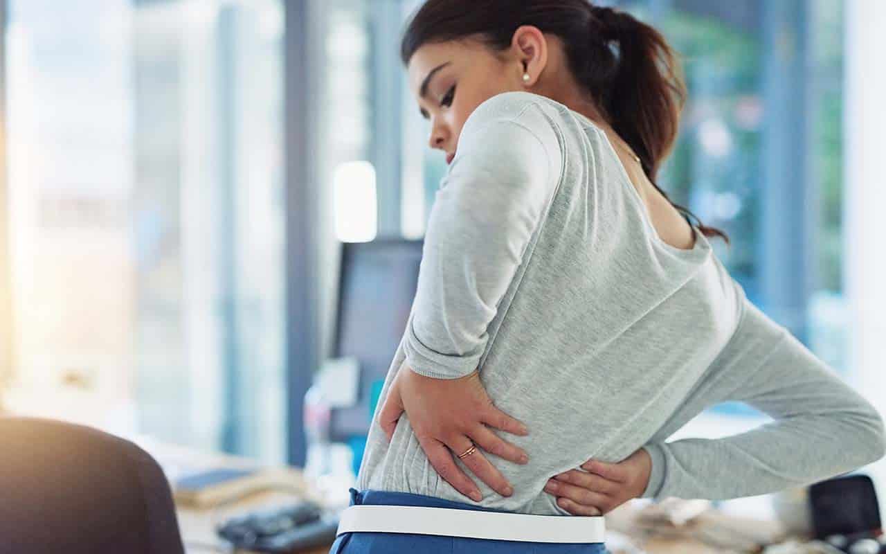 Mulher em seu escritório com dor na lombar - site Dr. Marcio Penna ortopedista especialista em coluna